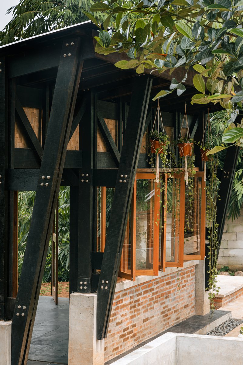 Exterior corner with black triangular timber bracing and brick half-wall beneath hanging plants