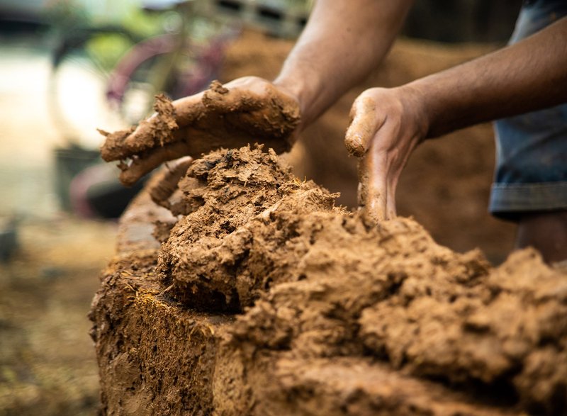 &nbsp; Close-up of raw earth mixture being applied, highlighting tactile construction methods.