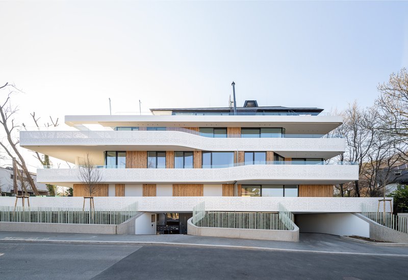Street view of the layered concrete balconies and timber cladding with bare winter trees overhead