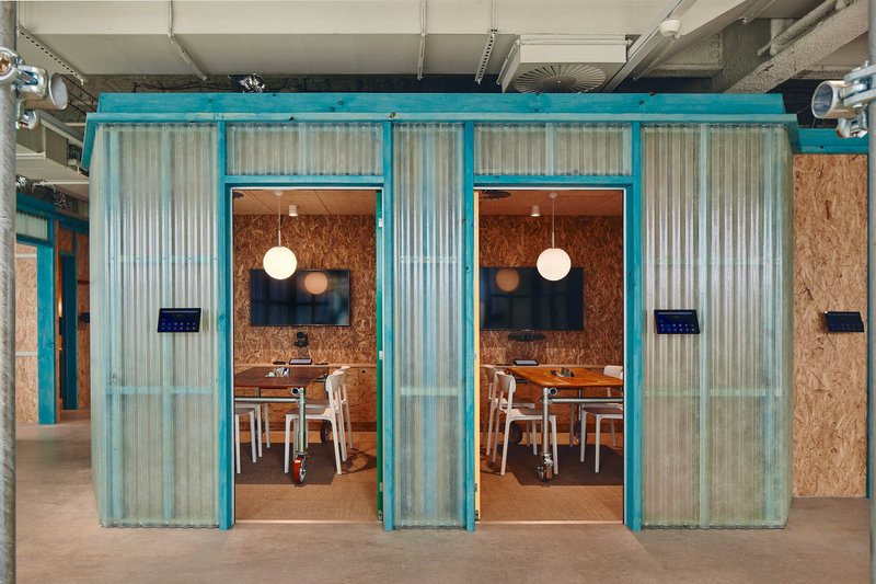 Meeting pods with turquoise corrugated metal frames and translucent curtains beneath exposed ceiling ducts
