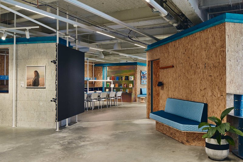 Open workspace with oriented strand board walls and turquoise steel trim under concrete ceiling