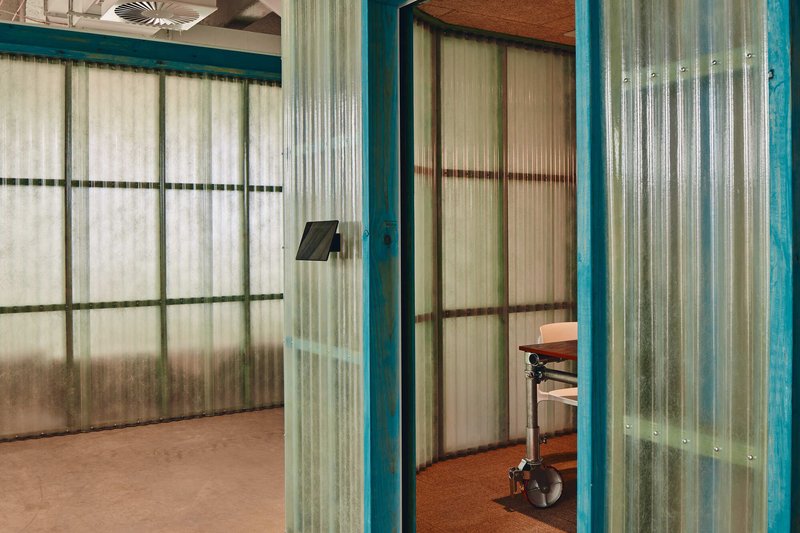 Close-up of translucent corrugated partitions in green steel frames with glimpse of workspace beyond