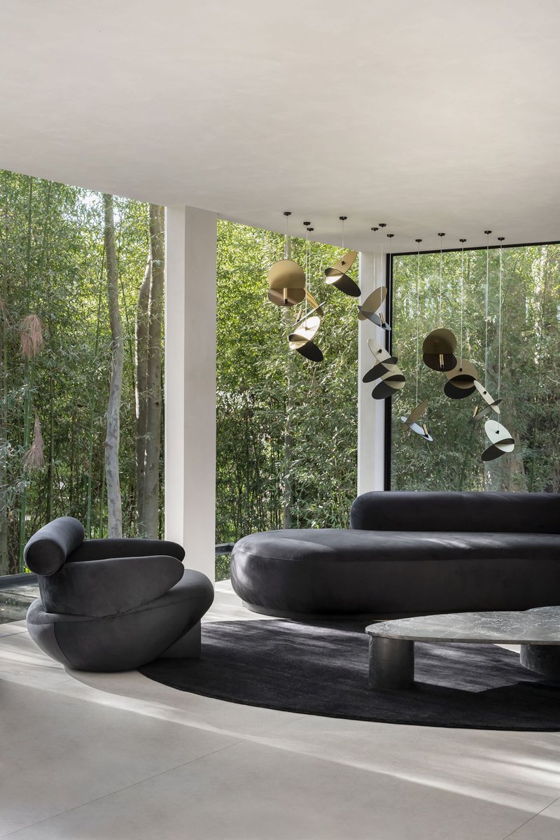 Living room with sculptural seating and pendant installation facing the glass walls and trees