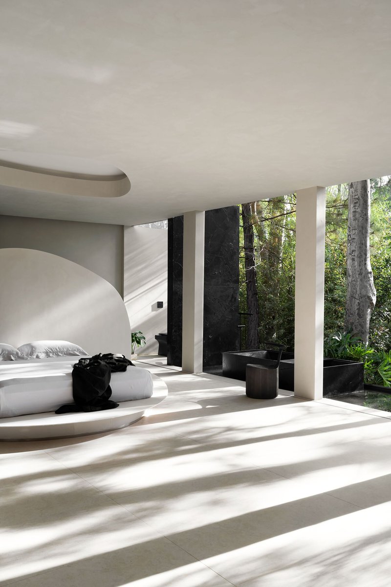 Bedroom platform with white bedding in striped morning sunlight from the forest edge