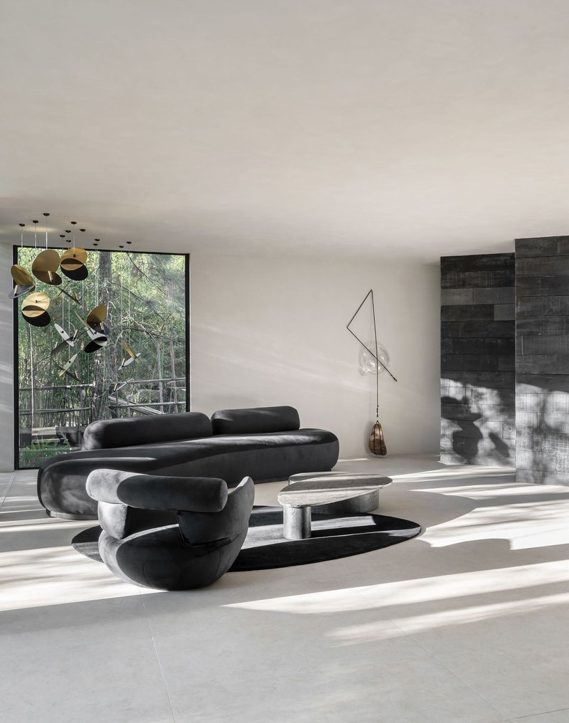 Living area with sculptural seating beneath recessed ceiling lights and view to charred timber courtyard wall