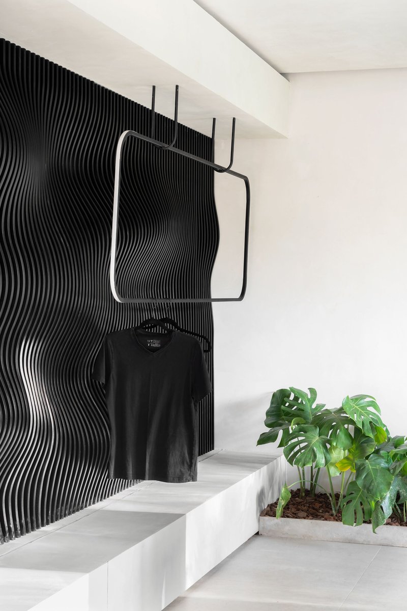 Black ribbed wall panel behind a steel clothing rack and white stepped seating with potted plants