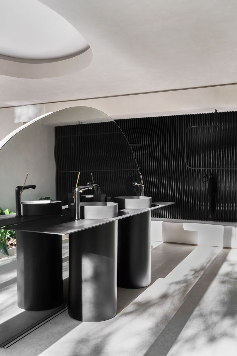Bathroom vanity with cylindrical black and white sinks against a ribbed black wall under curved ceiling vaults