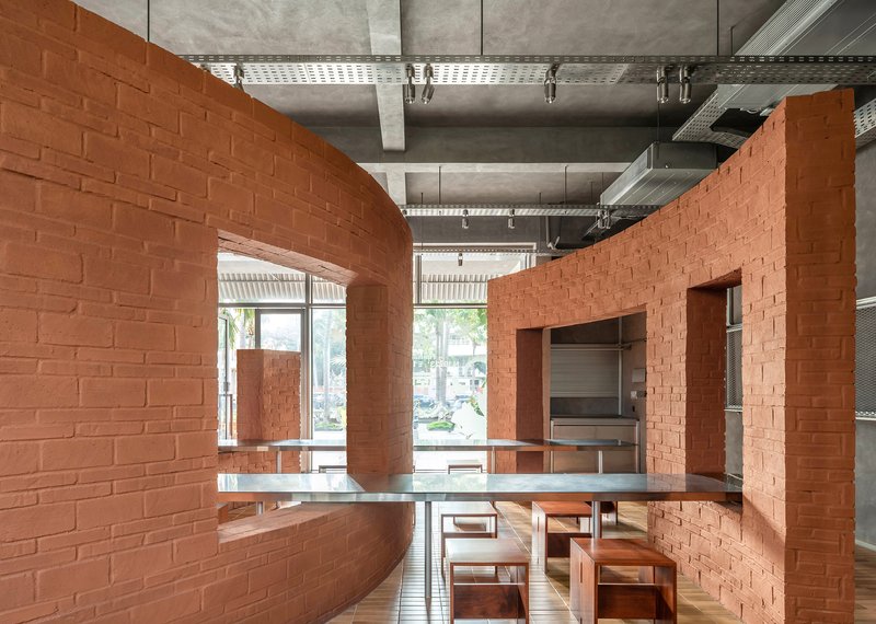 Curved terracotta brick walls enclosing a dining area with concrete ceiling and exposed ducts