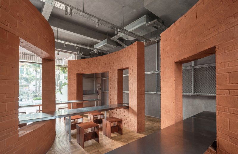 Interconnected terracotta brick volumes with large openings and shared dining table under raw concrete beams