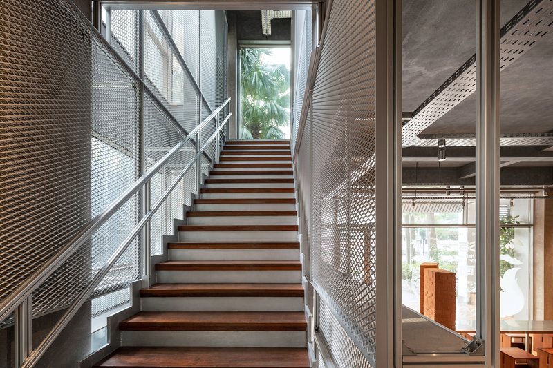 Timber-treaded staircase with expanded metal mesh railings and perforated metal walls filtering daylight