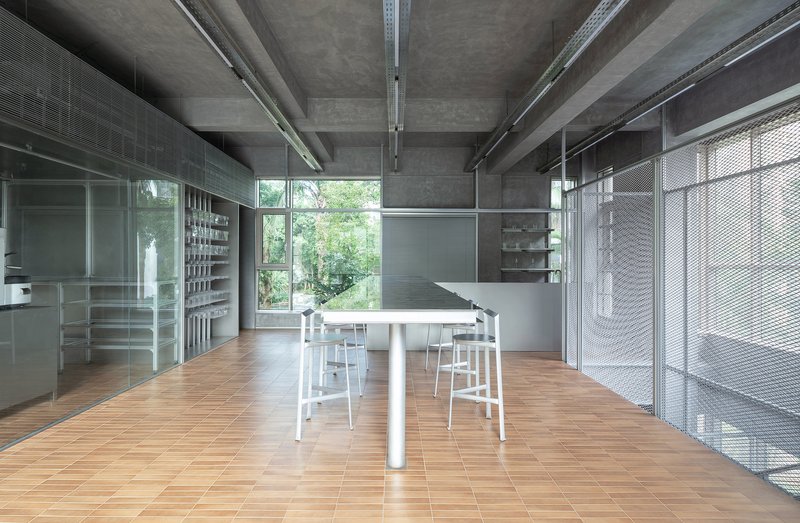 Long communal table surrounded by white stools beneath exposed concrete beams and service ducts
