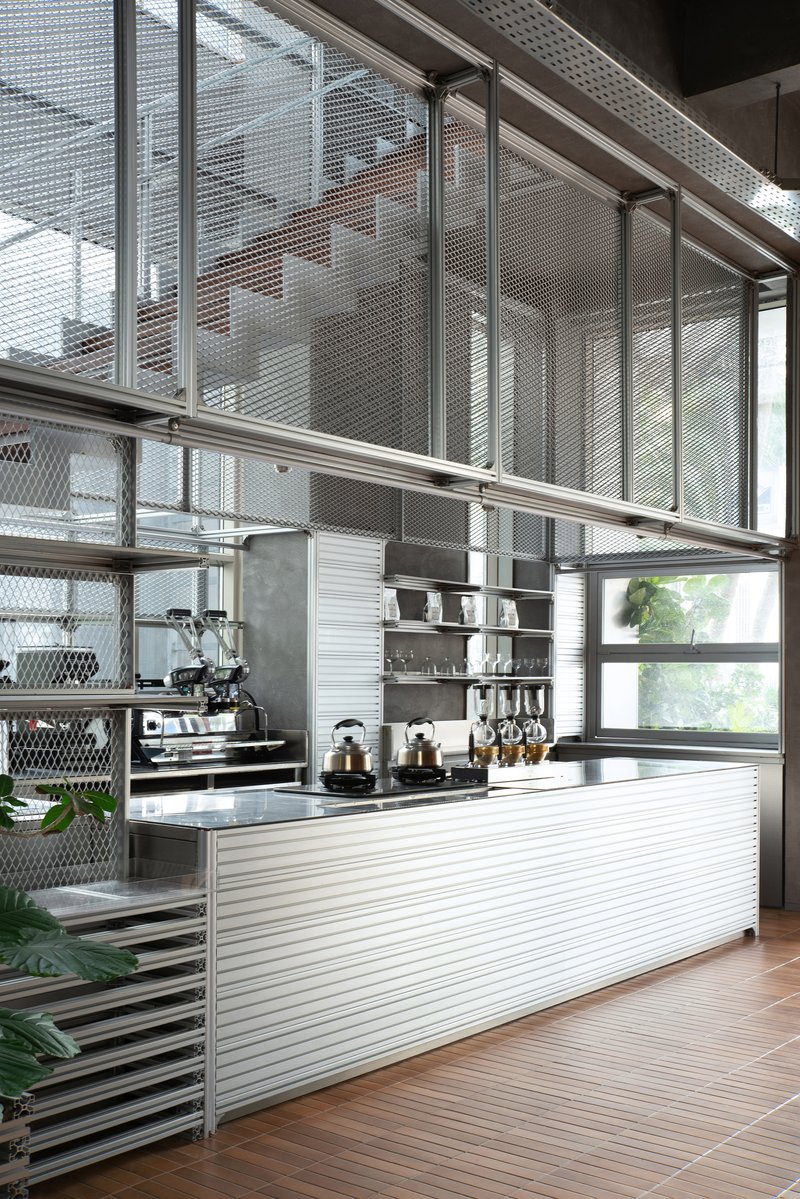 Cafe counter with corrugated metal cladding and espresso equipment beneath perforated metal mesh mezzanine railing