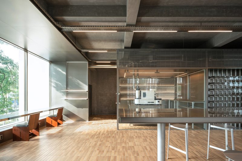 Double-height space with glass-enclosed office pods and orange lounge chairs near floor-to-ceiling windows