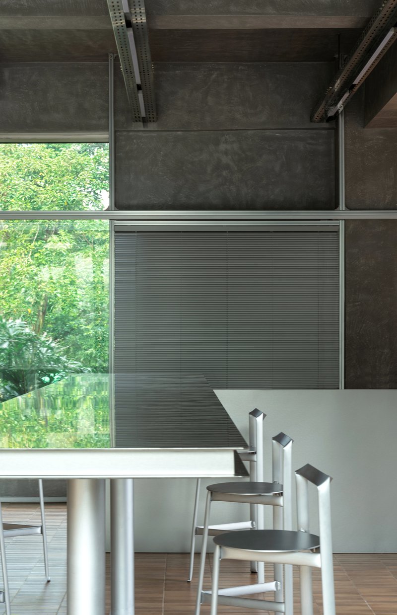 Detail of corrugated metal panel and stacked stools beside the communal table overlooking green foliage