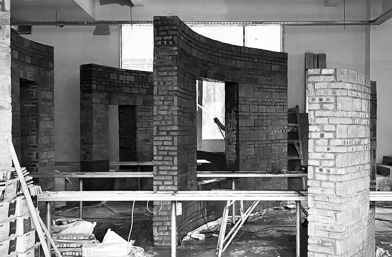 Construction view of curving brick partitions on raised steel platforms beneath exposed services