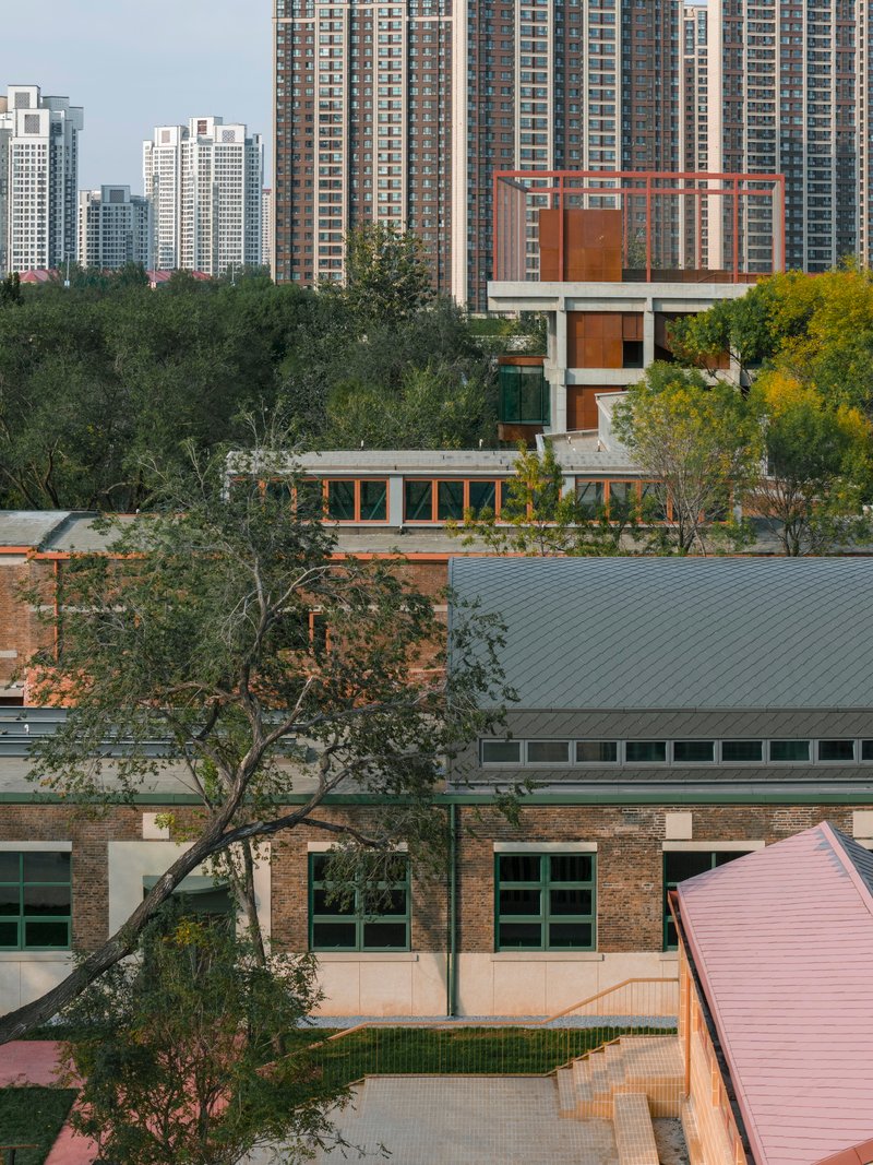 Elevated tower with rust-colored metal screens and glass walls emerging from treetops with apartment blocks behind