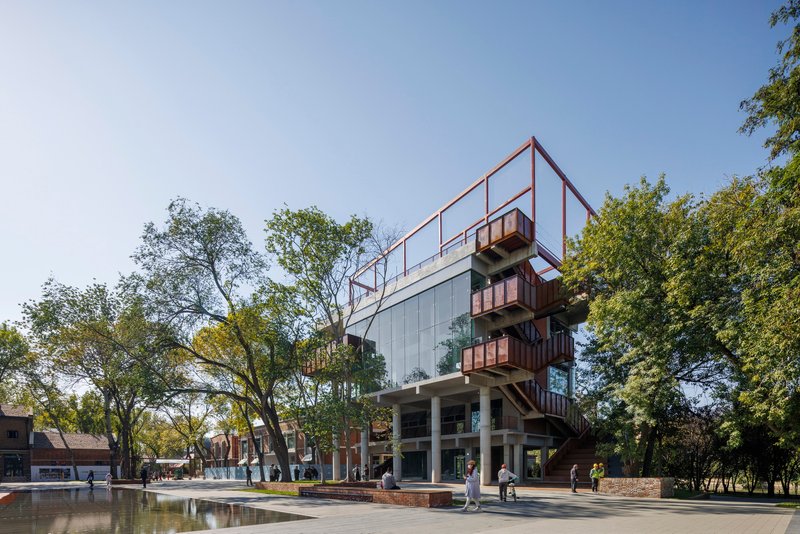 Elevated view of the multi-story structure with red steel frame and reflecting pool in the foreground