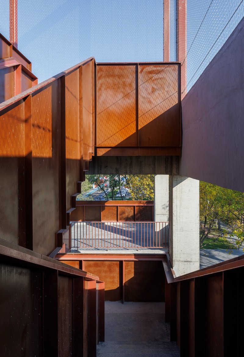 Framed view through stacked weathered steel balconies and concrete floor slabs at dusk