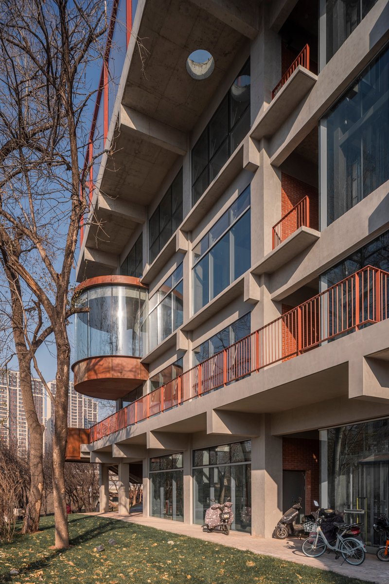 Facade detail showing concrete structure, glass elevator shaft, and corrugated metal balcony railings in afternoon light