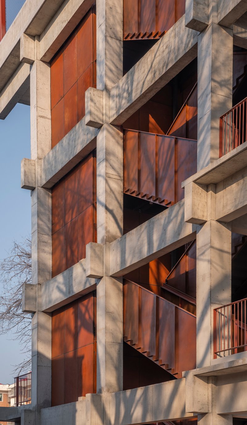 Facade detail showing diagonal tree shadows cast across weathered steel panels and concrete structural grid