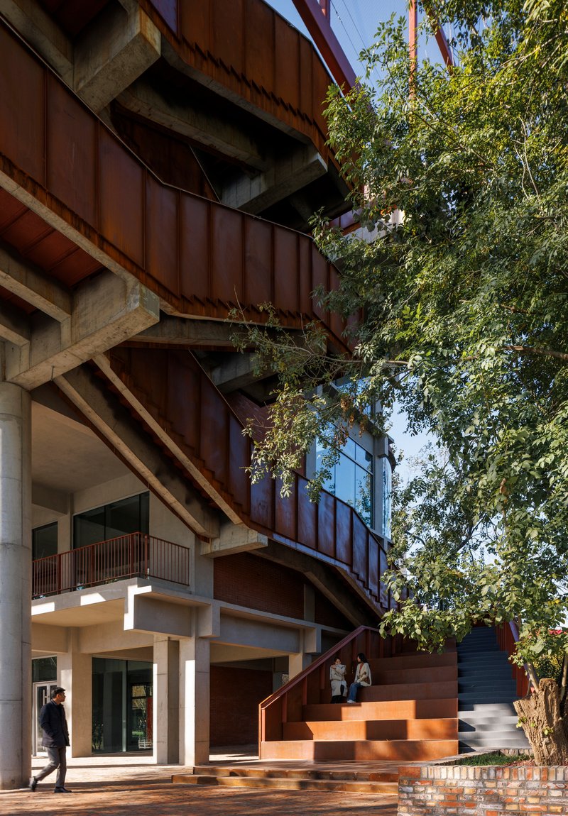 Ground level entrance with stepped weathered steel platform and concrete columns beneath cantilevered upper floors