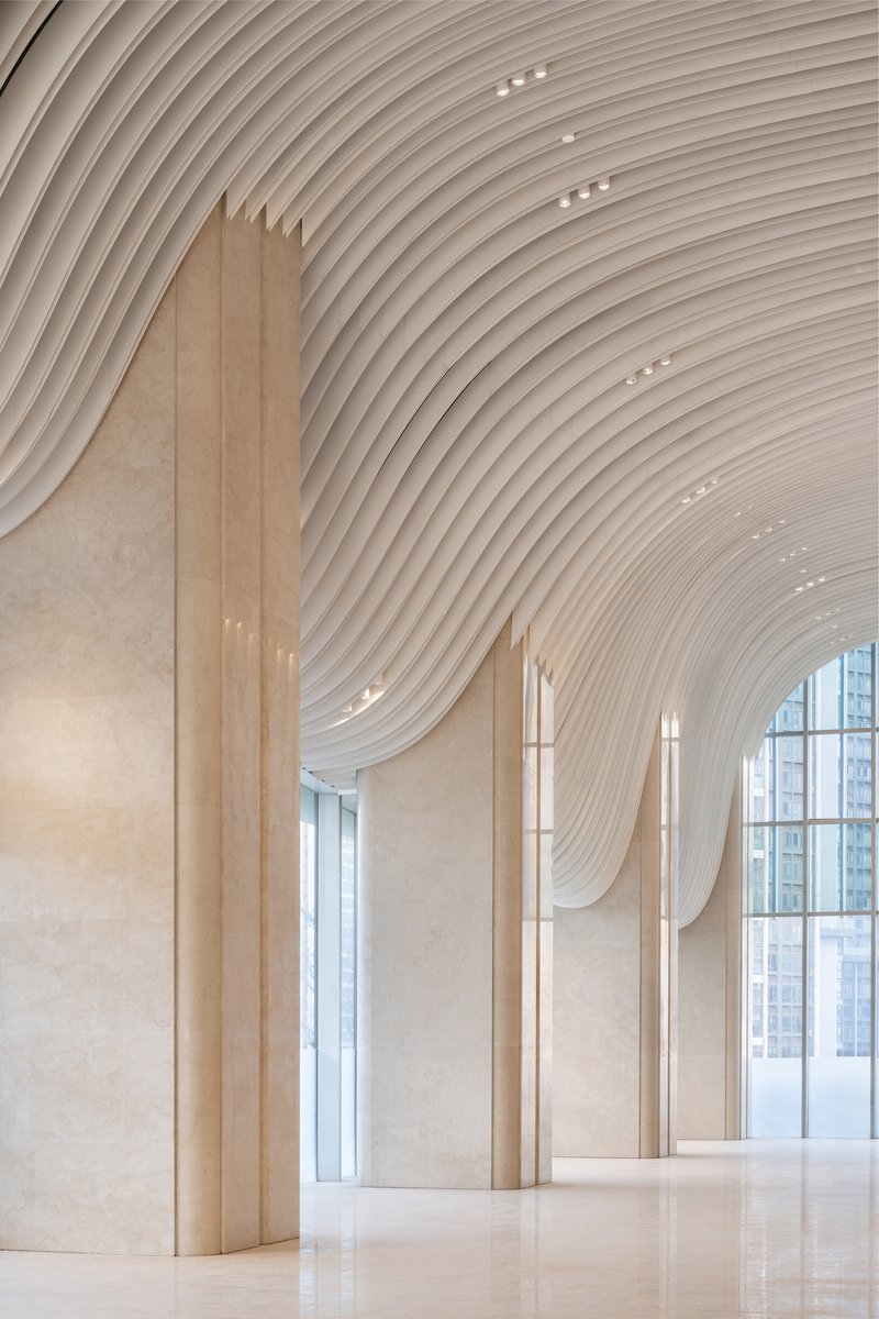 Close-up of stone column meeting the flowing ribbed ceiling with tall glazed curtain wall beyond