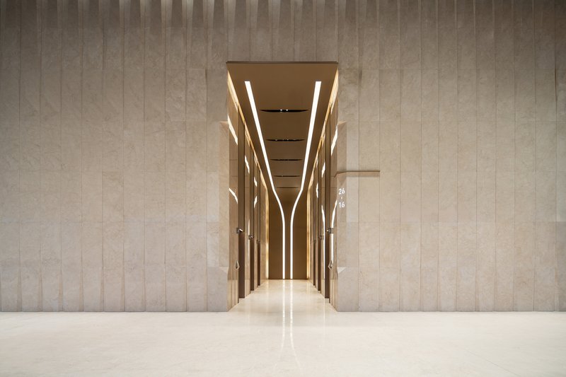 Elevator lobby framed by illuminated vertical mullions and polished stone floor reflecting overhead lighting