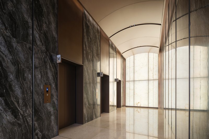 Elevator lobby with dark veined stone walls and arched translucent glass partition under barrel vault ceiling