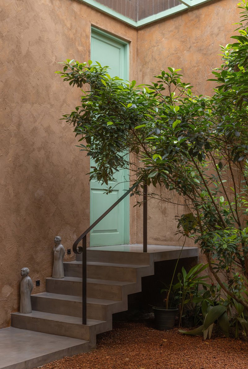 Exterior staircase with steel railing ascending to a mint green door beside a young tree in the courtyard