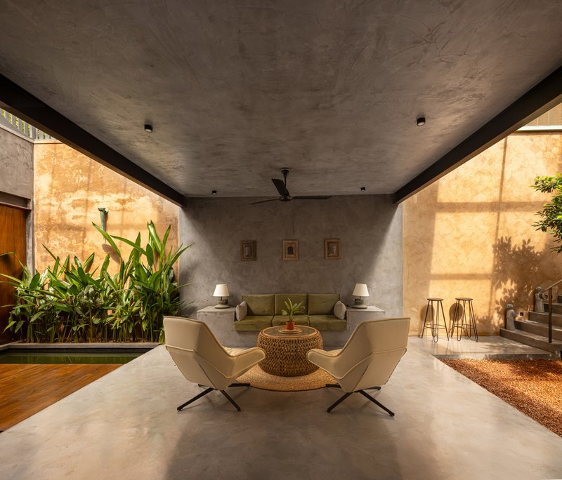 Living area with concrete ceiling and walls where afternoon sun casts shadows through adjacent plants