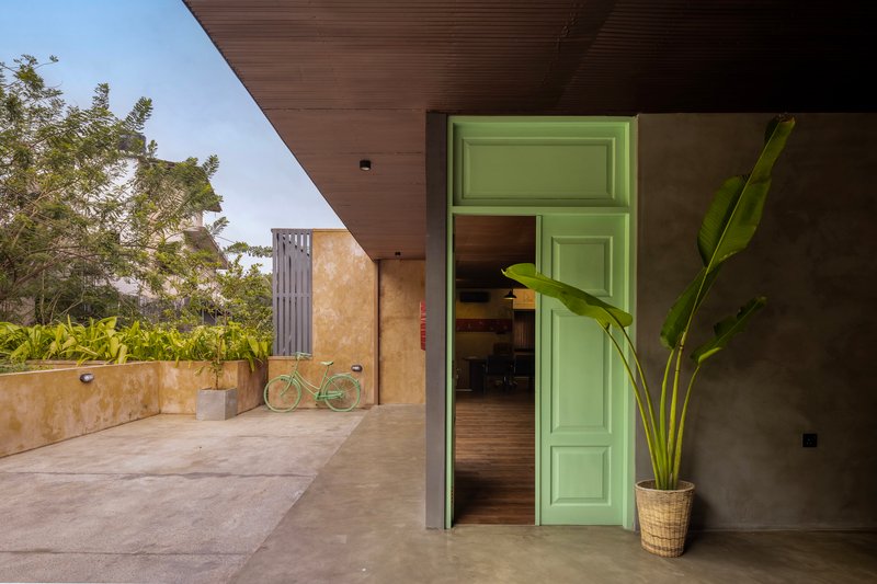 Covered terrace with green paneled door opening to interior and a bicycle leaning against the wall