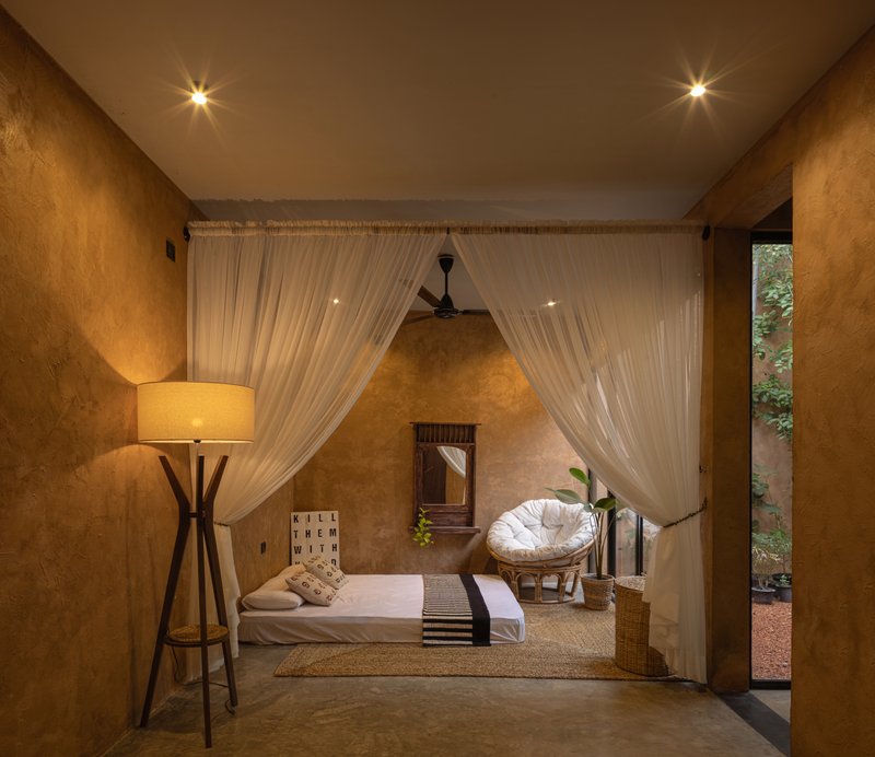 Bedroom framed by sheer white curtains with view to exterior courtyard at dusk