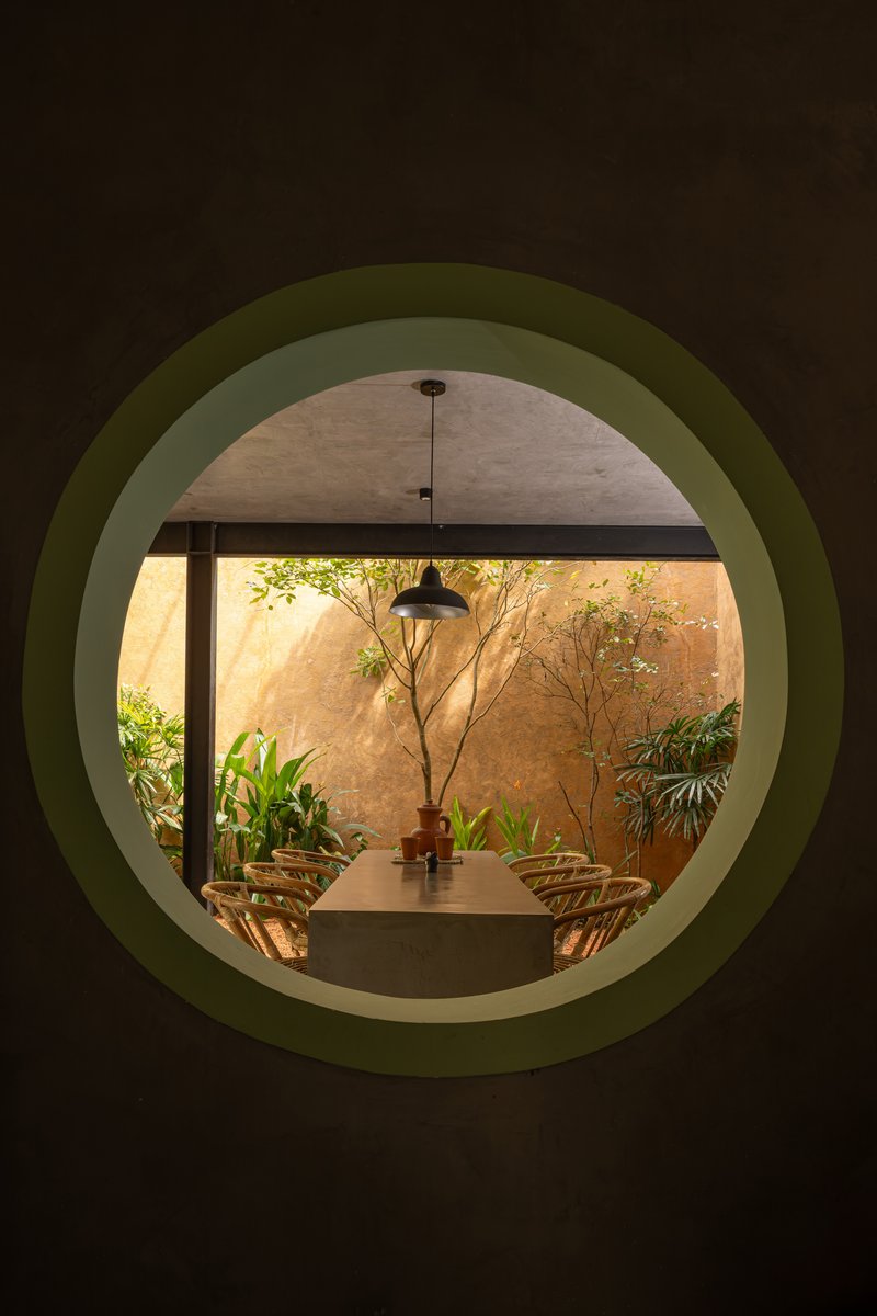 View through circular green portal to dining table and sunlit courtyard with tree