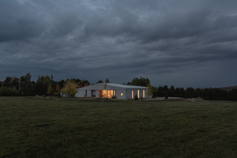 Night view of the illuminated residence across a dark meadow under heavy storm clouds