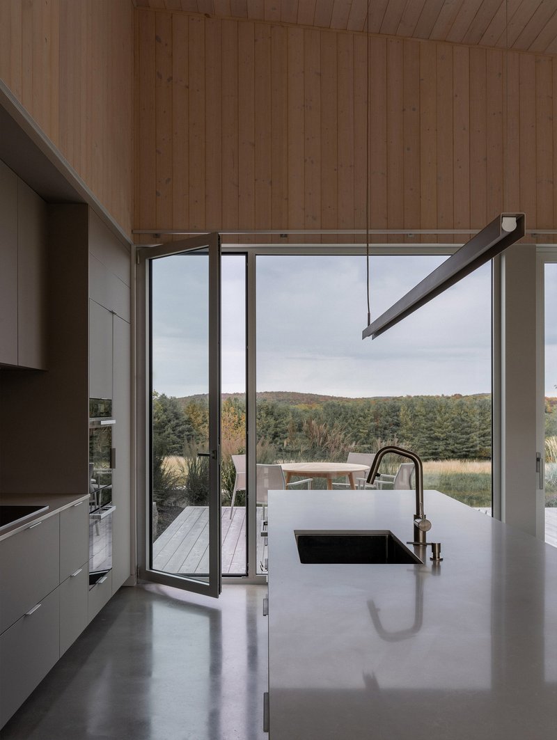 Kitchen island with integral sink facing narrow glass door and distant wooded hillside under overcast sky