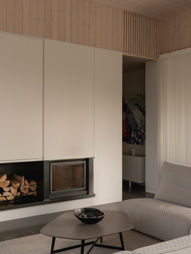 Living room fireplace with stacked firewood storage beneath a timber-lined ceiling volume