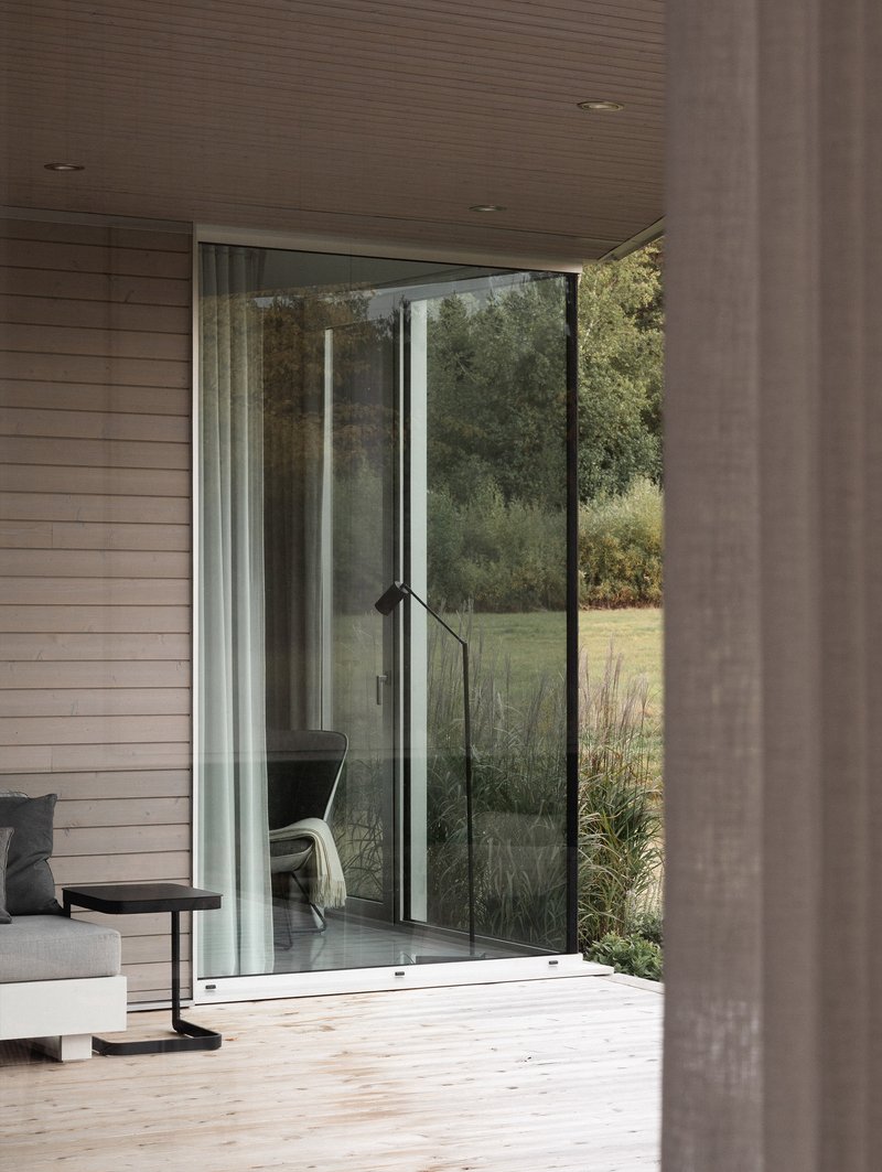 Open sliding glass door connecting timber deck to interior and overlooking grassy meadow with trees