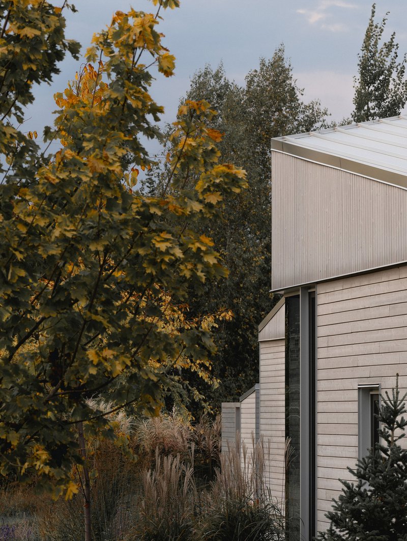 Exterior view of the ribbed metal upper volume rising above horizontal siding amid autumn foliage