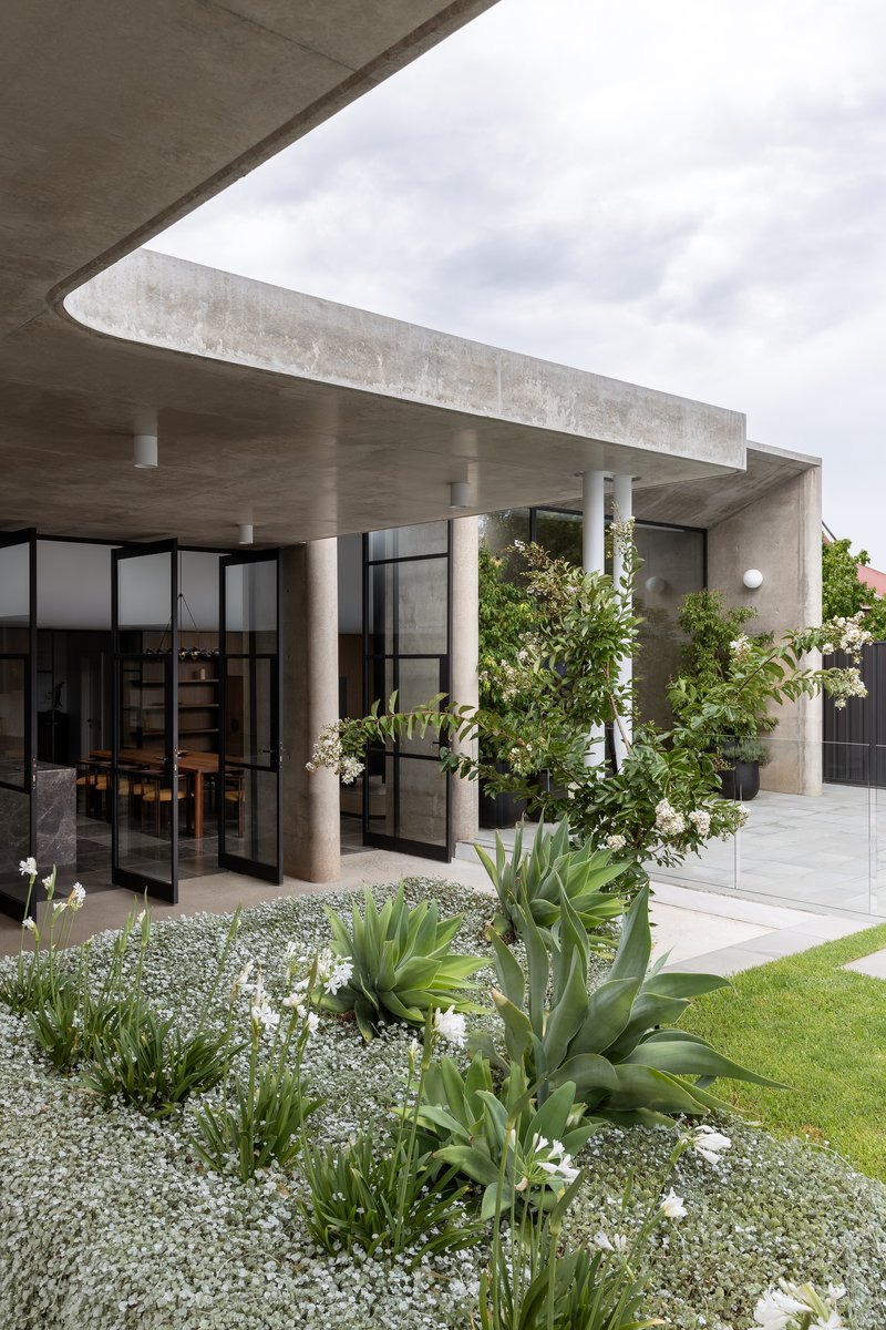 Concrete roof overhang supported by cylindrical columns above planted bed with agave and white gravel