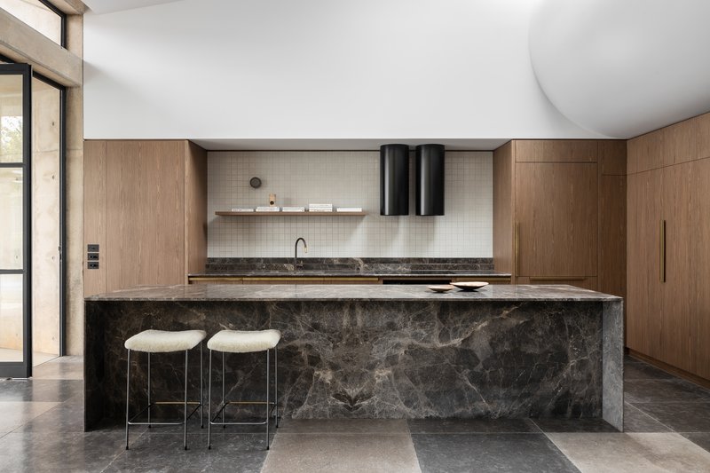 Kitchen island clad in dark stone with timber cabinetry and cylindrical black pendant lights above