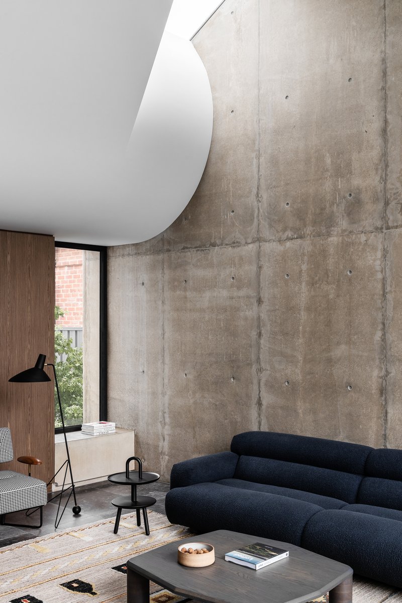 Living room with board-formed concrete wall and curved white ceiling element above seating