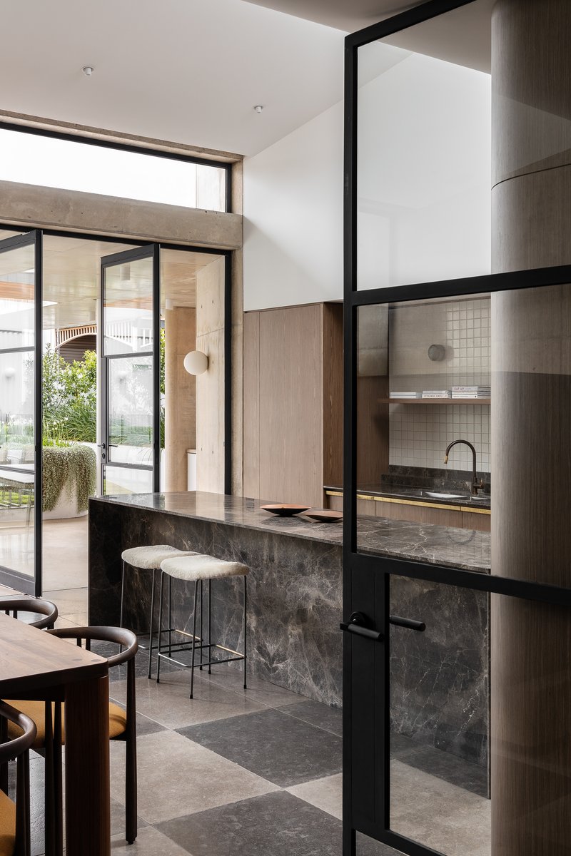 View through steel-framed glass partition to kitchen with stone island and garden beyond