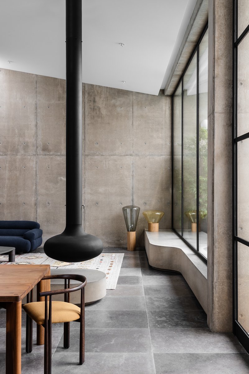 Double-height living space with board-formed concrete walls and floor-to-ceiling steel-framed glazing along one side