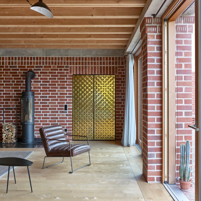 Interior living space with exposed timber ceiling, red brick walls, brass textured panels and leather chair
