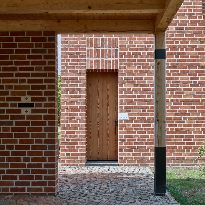 Timber entry door recessed in brick wall with exposed wood rafters overhead and cobblestone paving