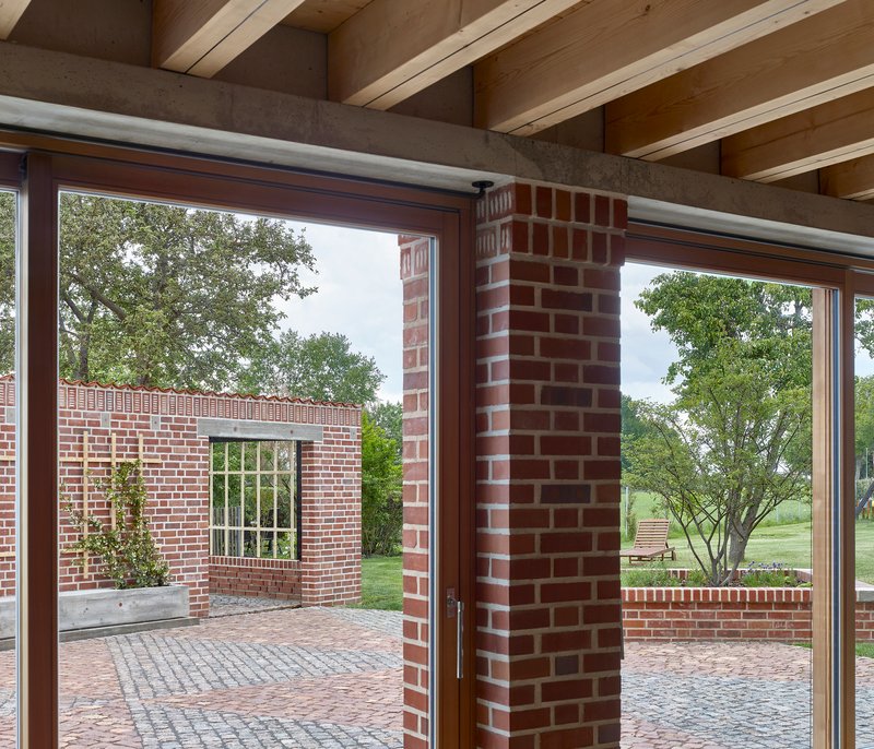 Interior view through glazed corner opening showing exposed timber joists and brick columns framing the courtyard