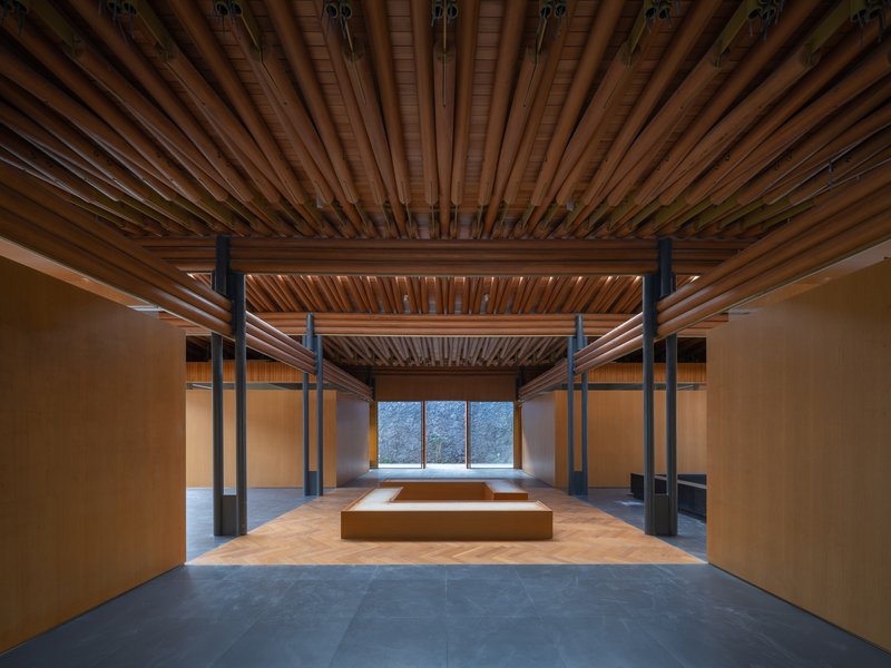 Gallery interior with radial timber ceiling panels and black steel columns framing a distant window
