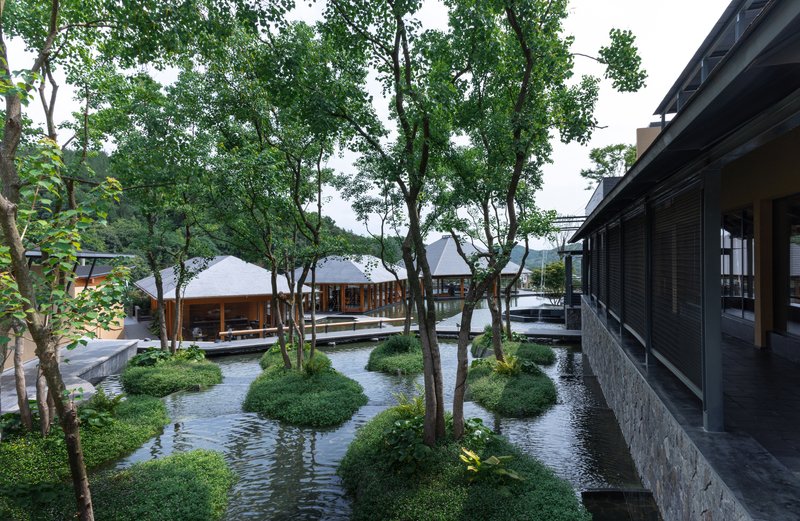 Water courtyard with planted islands, mature trees, and covered walkways under overcast sky
