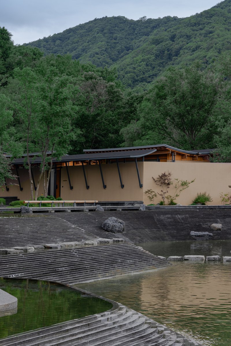 Exterior showing angled steel columns supporting a low-pitched roof beside a stepped stone water feature and reflecting pool