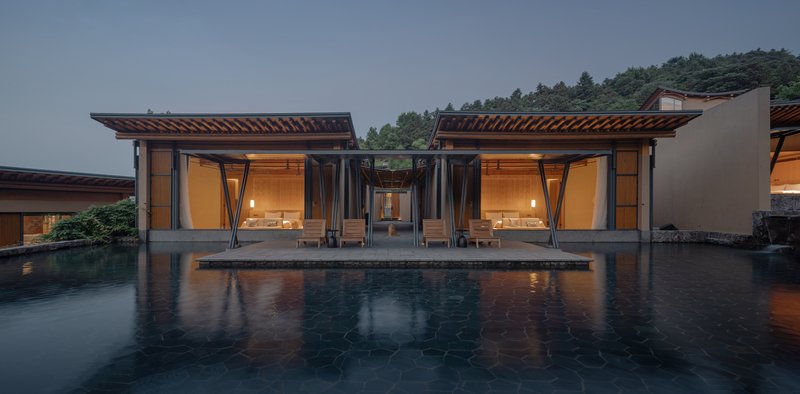 Twin pavilions with exposed timber roofs flanking a reflecting pool at dusk